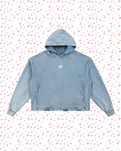 Blue hoodie with a small white logo on a pink background with heart patterns
